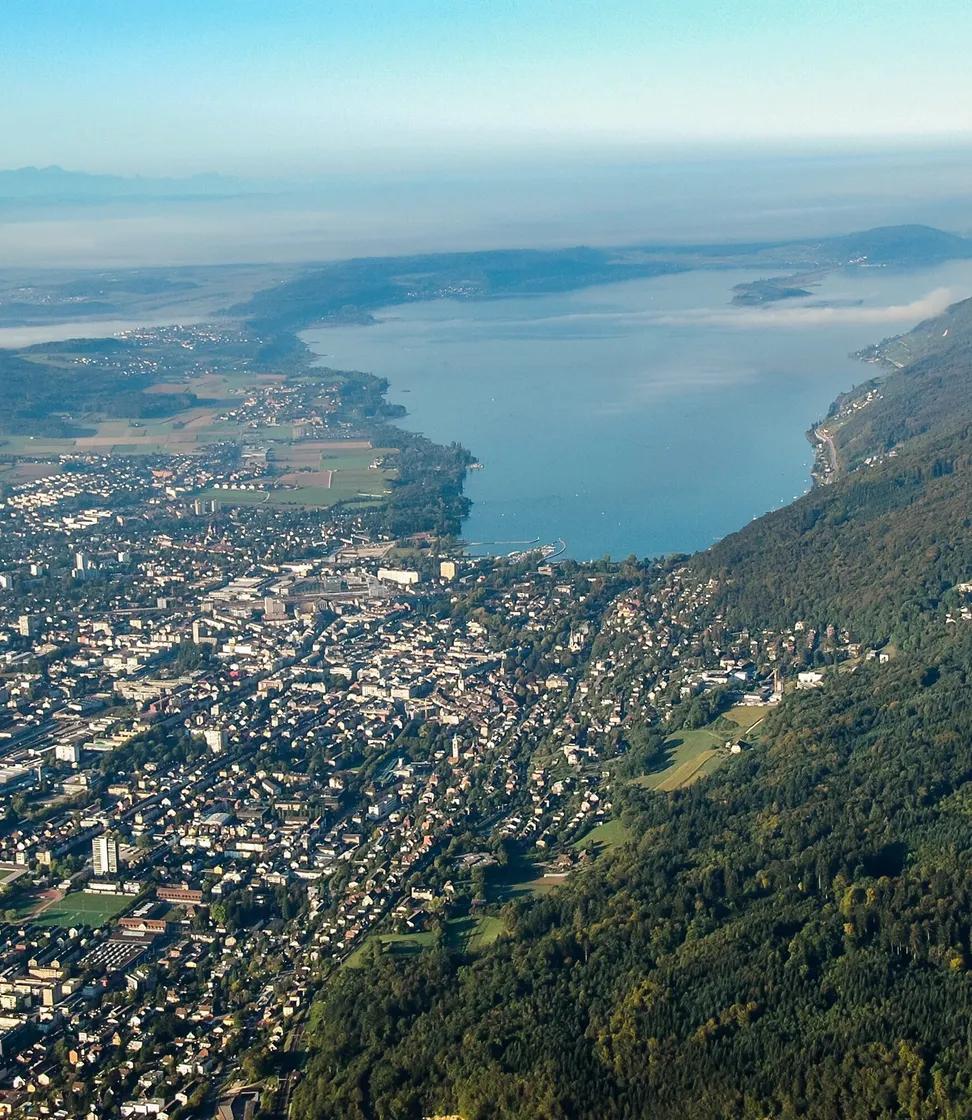 Auf dem Bild ist eine Flugaufnahme von Biel zu sehen, worauf man einen schönen Blick auf die Stadt und den Bielersee hat.